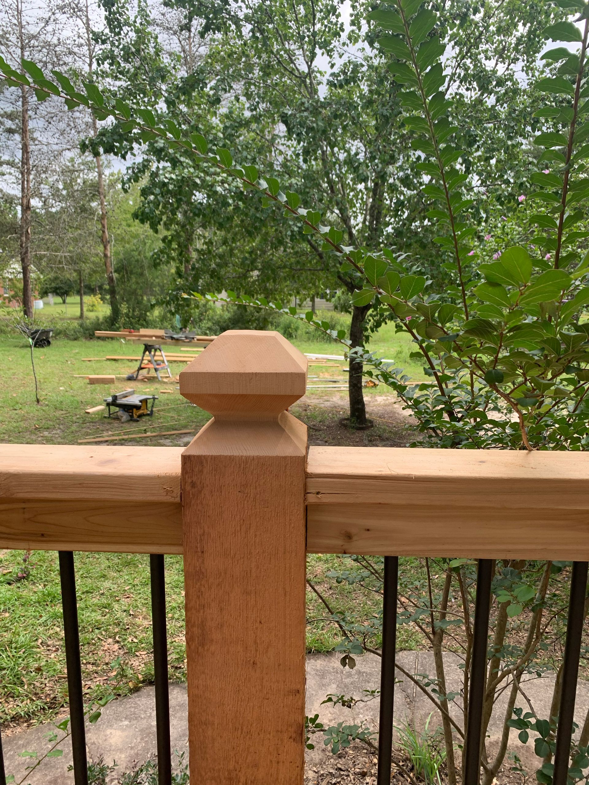 Wooden deck railing with a view of a backyard, trees, and construction in the distance.
