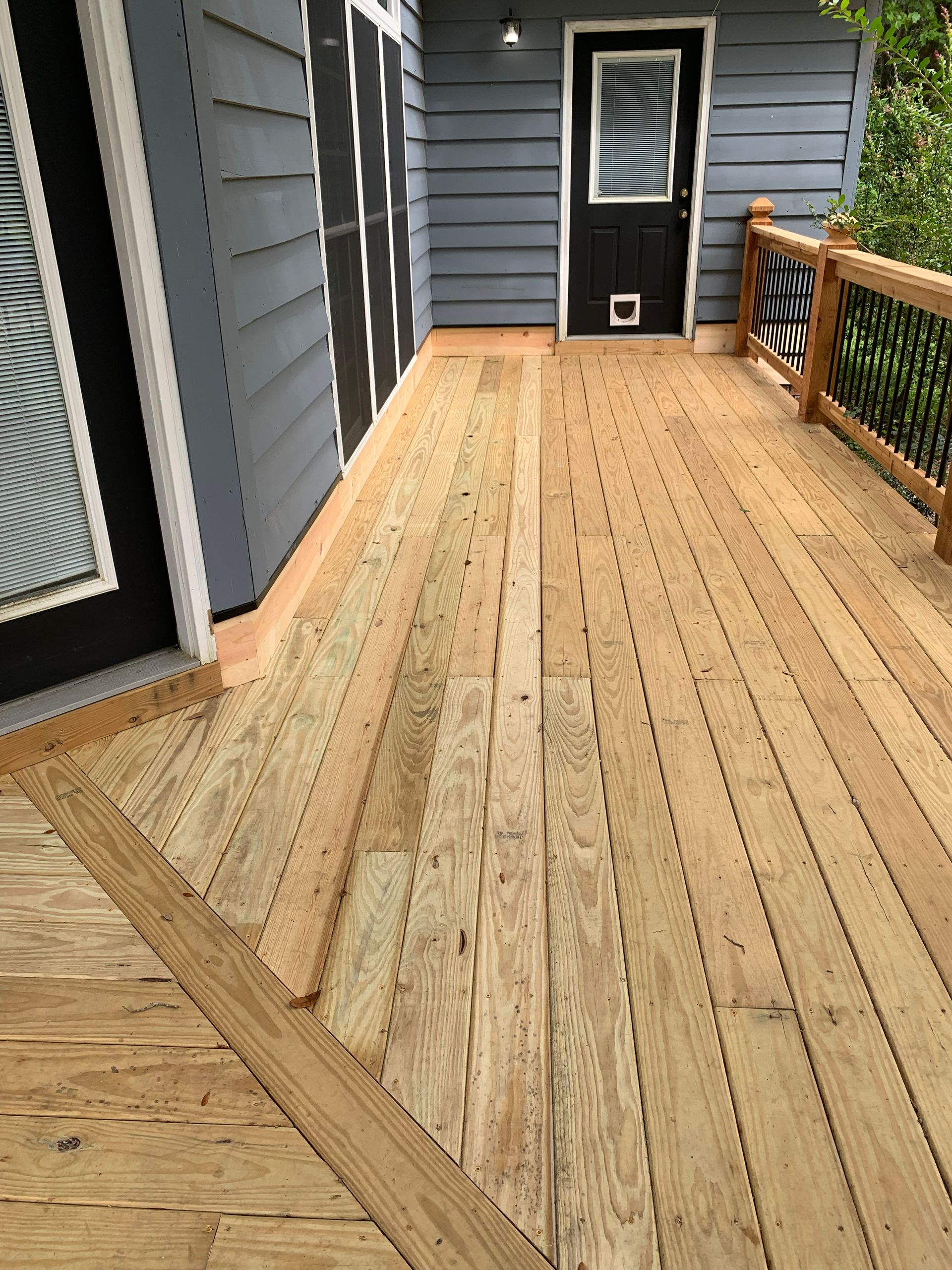 Wooden deck with a dark blue house and door, black railing, and a dog door.