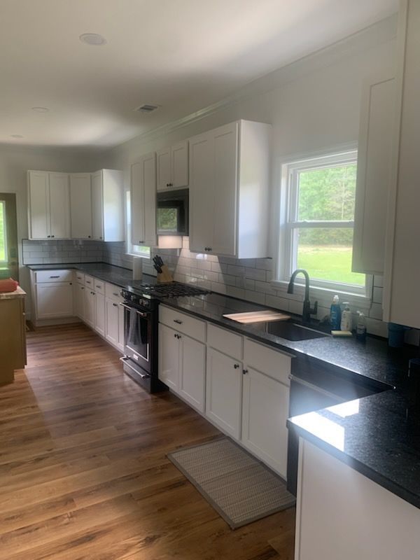 White kitchen with dark countertops, wood floors, and a window.