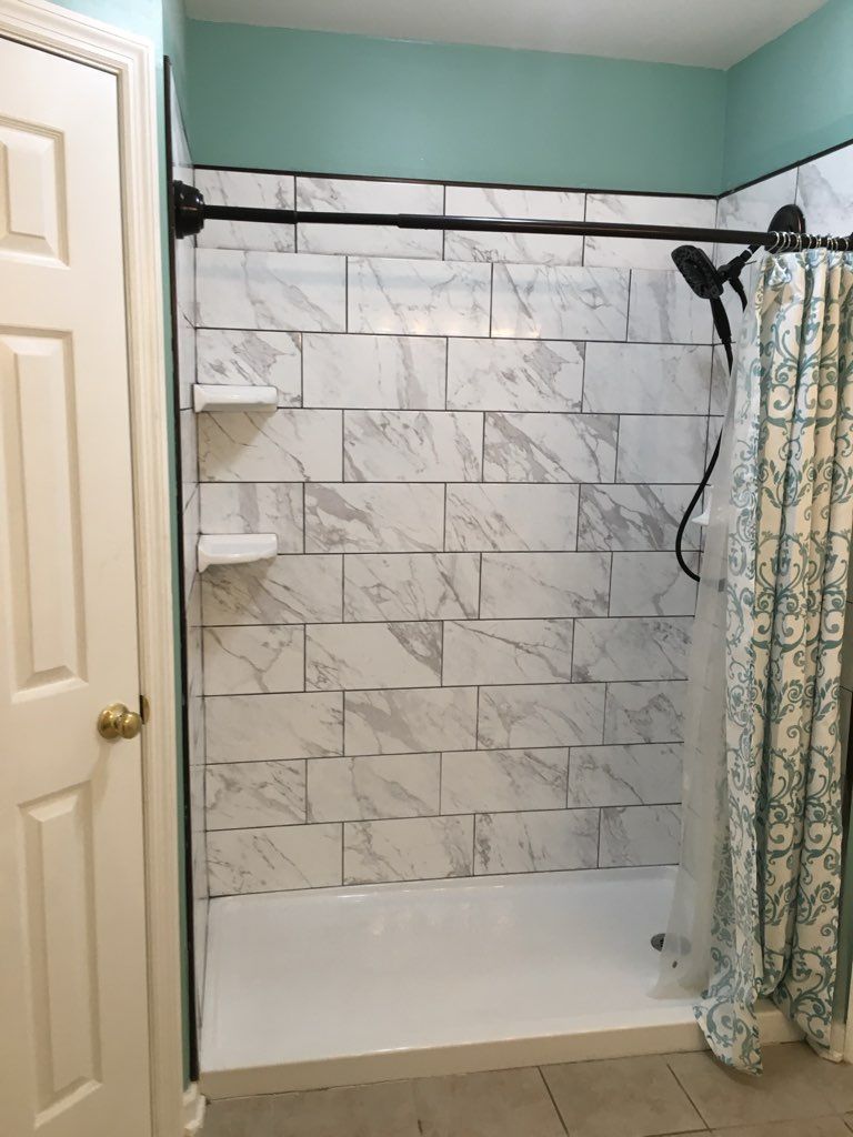 Bathroom with white marble-look tiled shower, black shower rod and fixtures, and teal walls.
