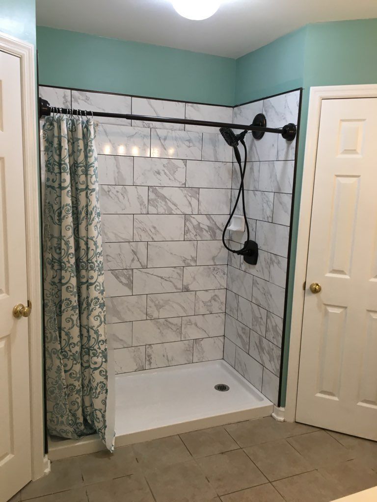 Bathroom with a marble-tiled shower stall, shower curtain, black shower fixtures, and two white doors.