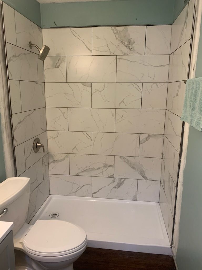 A small, white-tiled shower stall next to a toilet in a bathroom with a light blue wall.