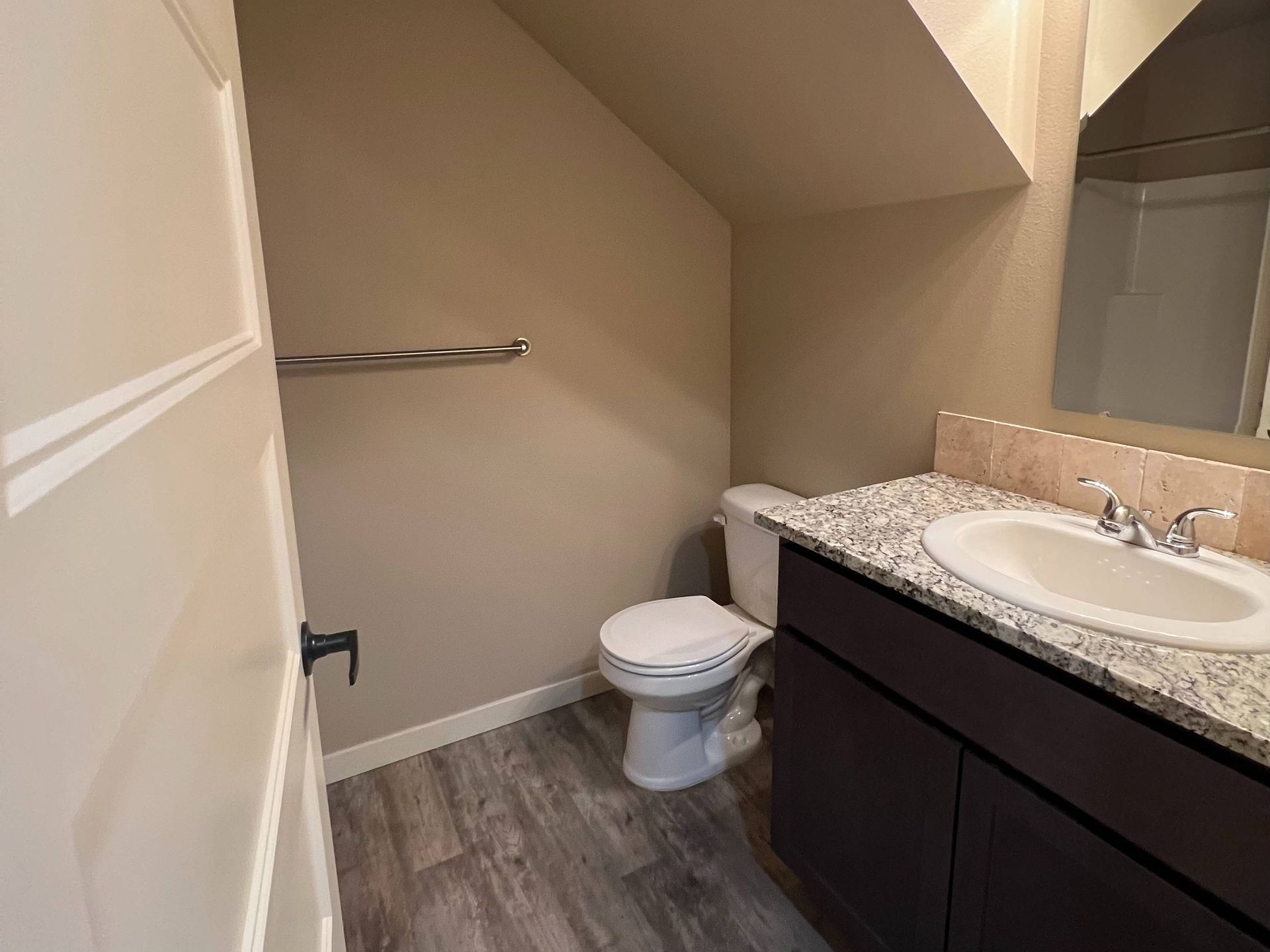 Bathroom with a toilet, vanity with granite countertop, and gray wood-look flooring.