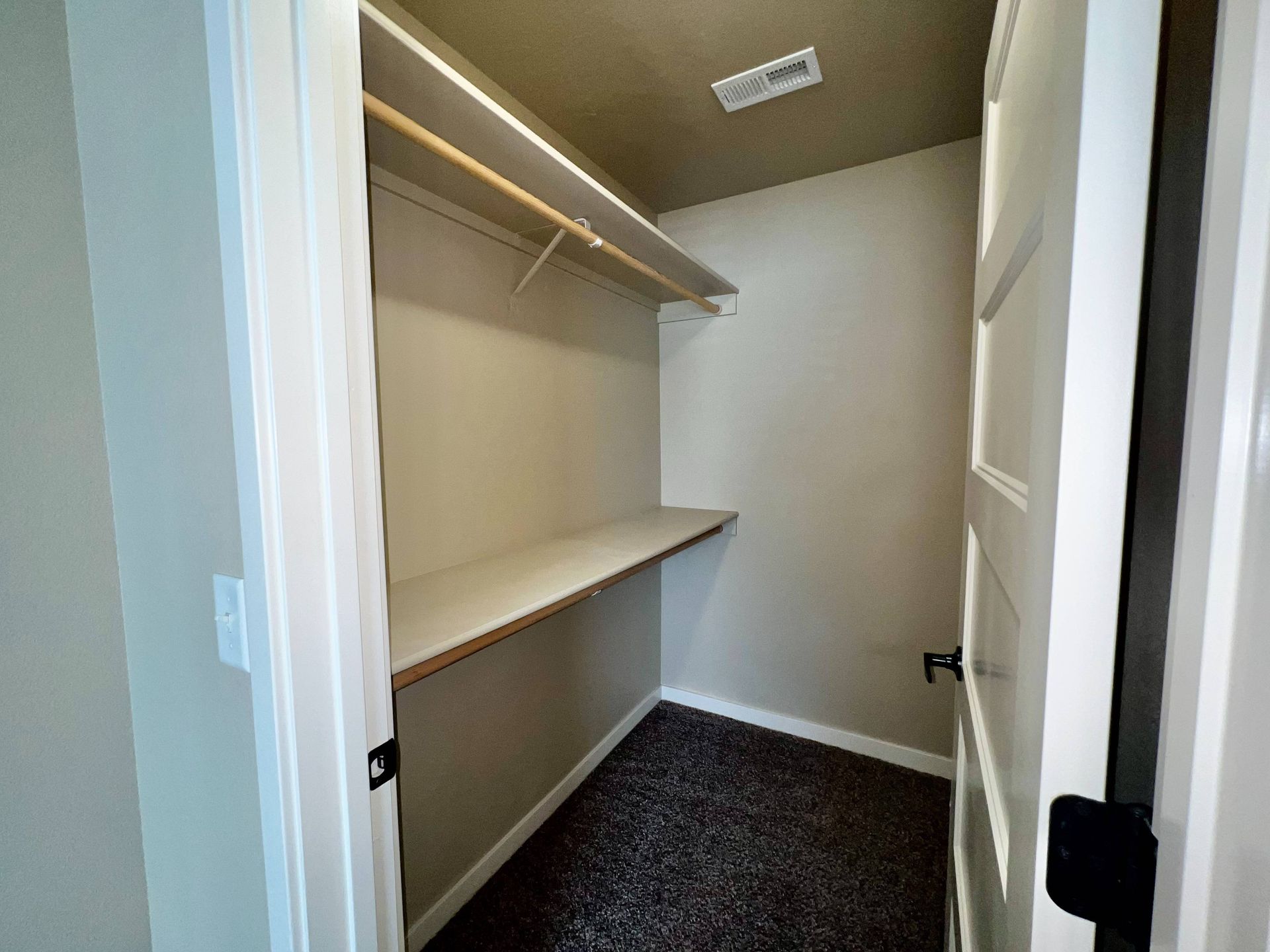 Empty closet with white shelves, rod, and door. Carpeted floor.