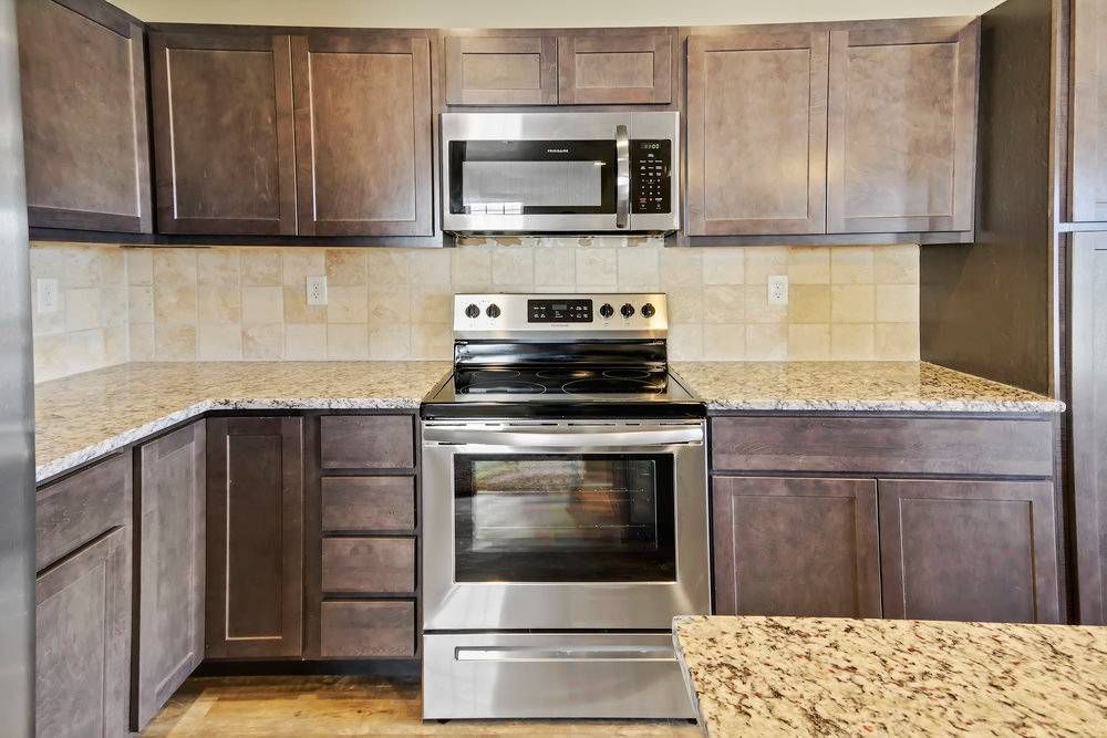 Kitchen with dark brown cabinets, stainless steel appliances, and beige tile backsplash.