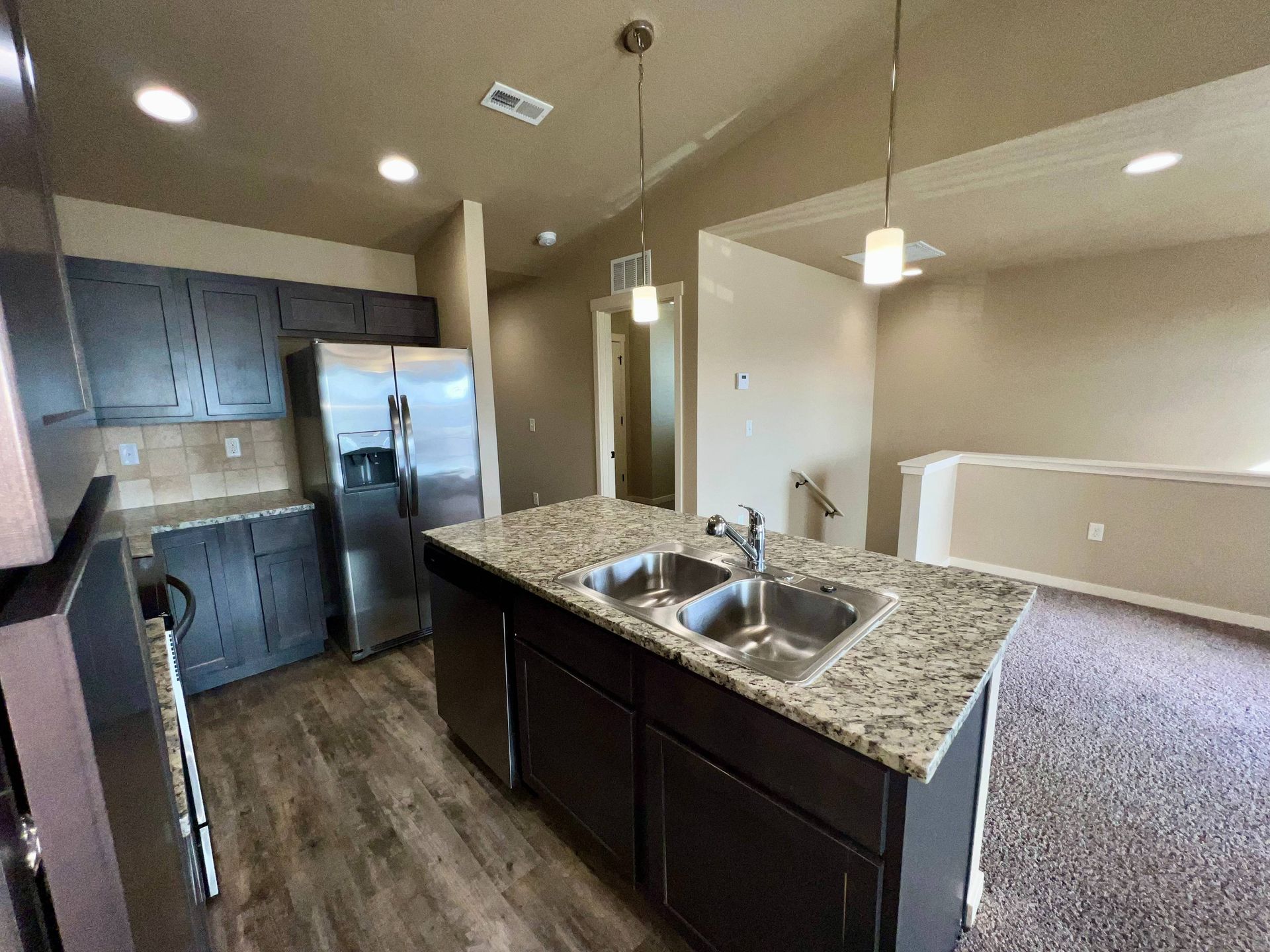 Kitchen with island, dark cabinets, stainless steel appliances, and wood-look flooring.