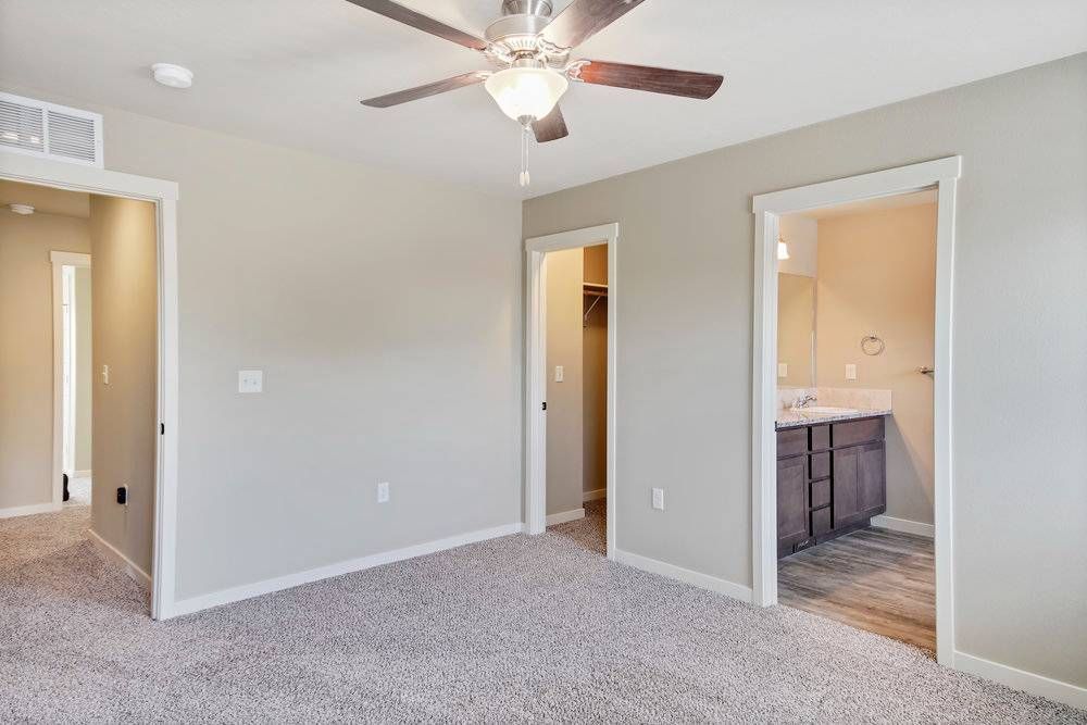 Bedroom with carpet, three doorways, ceiling fan, and tan walls.