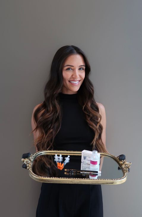 Woman in a black dress holding a decorative tray with desserts, standing against a plain gray background