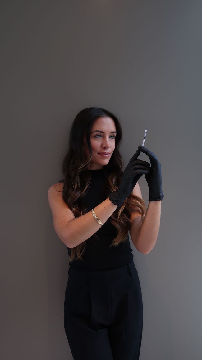 Woman in black gloves posing with a metallic object against a plain gray background