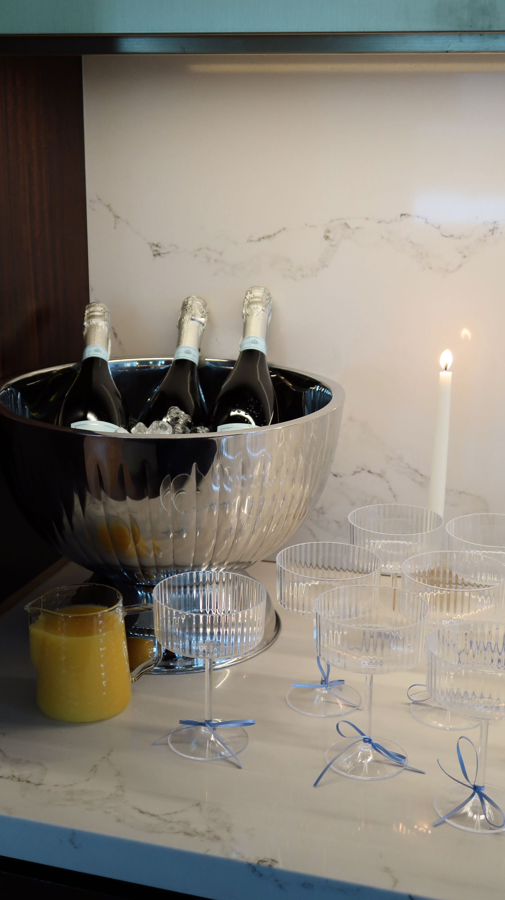 Champagne bottles in a silver ice bucket beside glasses and a lit candle on a table