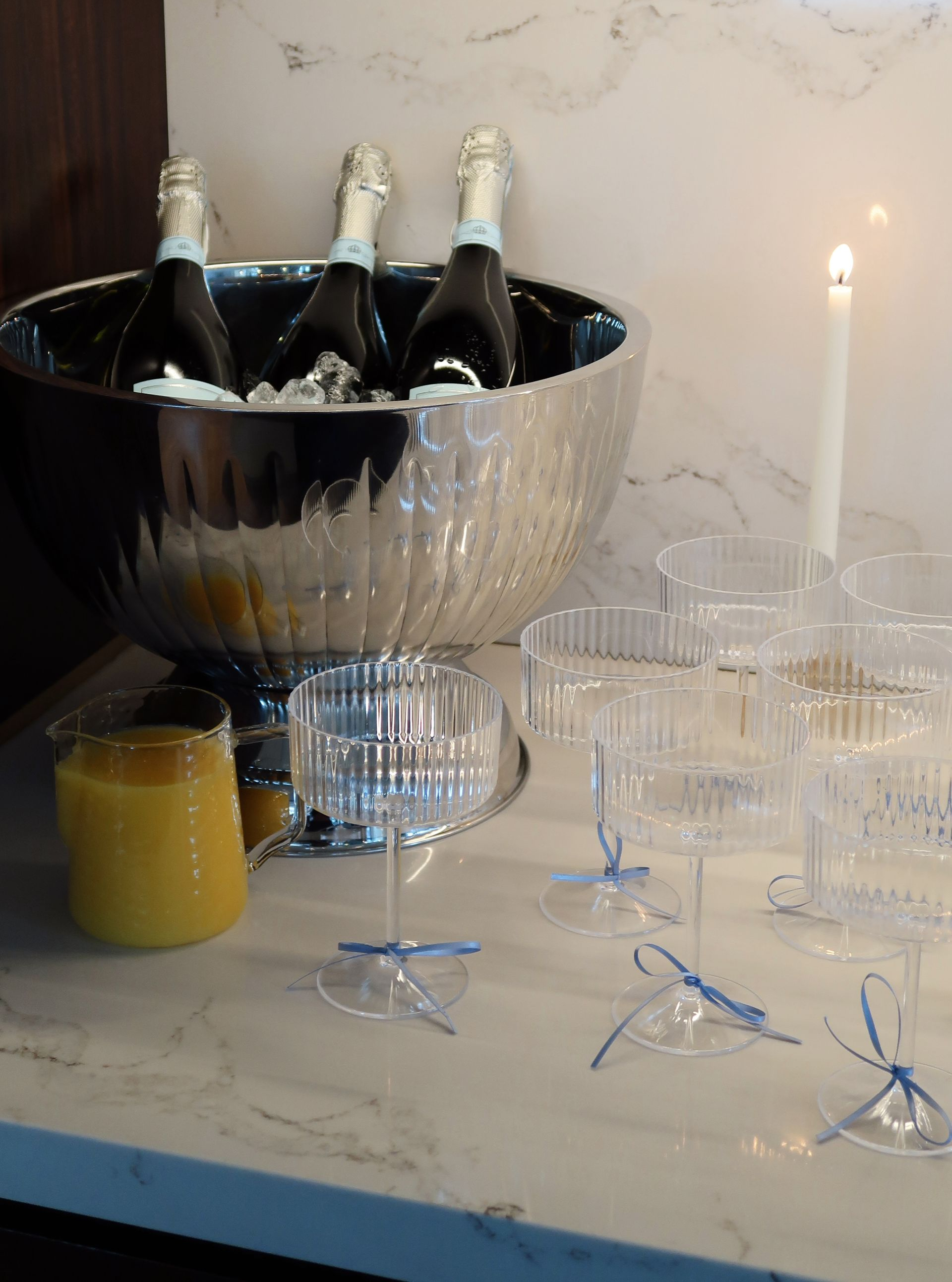 Champagne bottles in a silver ice bucket beside glasses, a candle, and a yellow drink on a table