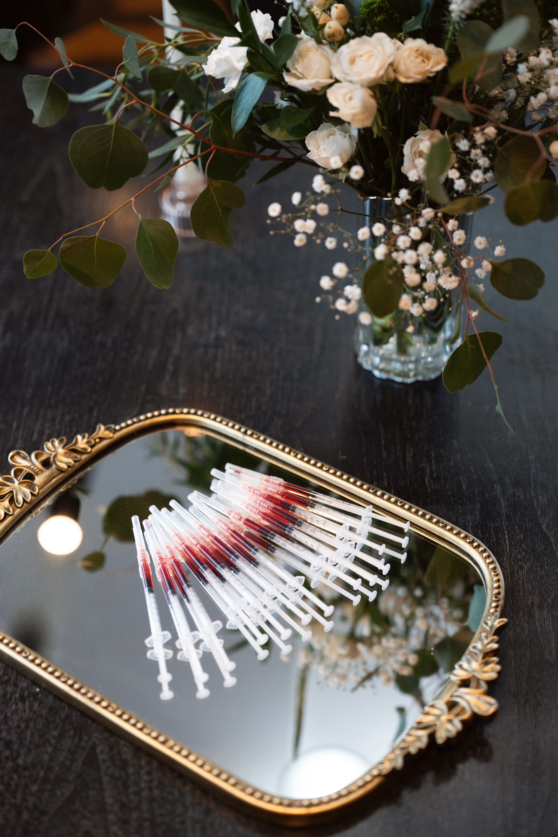 Decorative makeup brushes arranged on a gold mirror beside a floral bouquet on a dark table