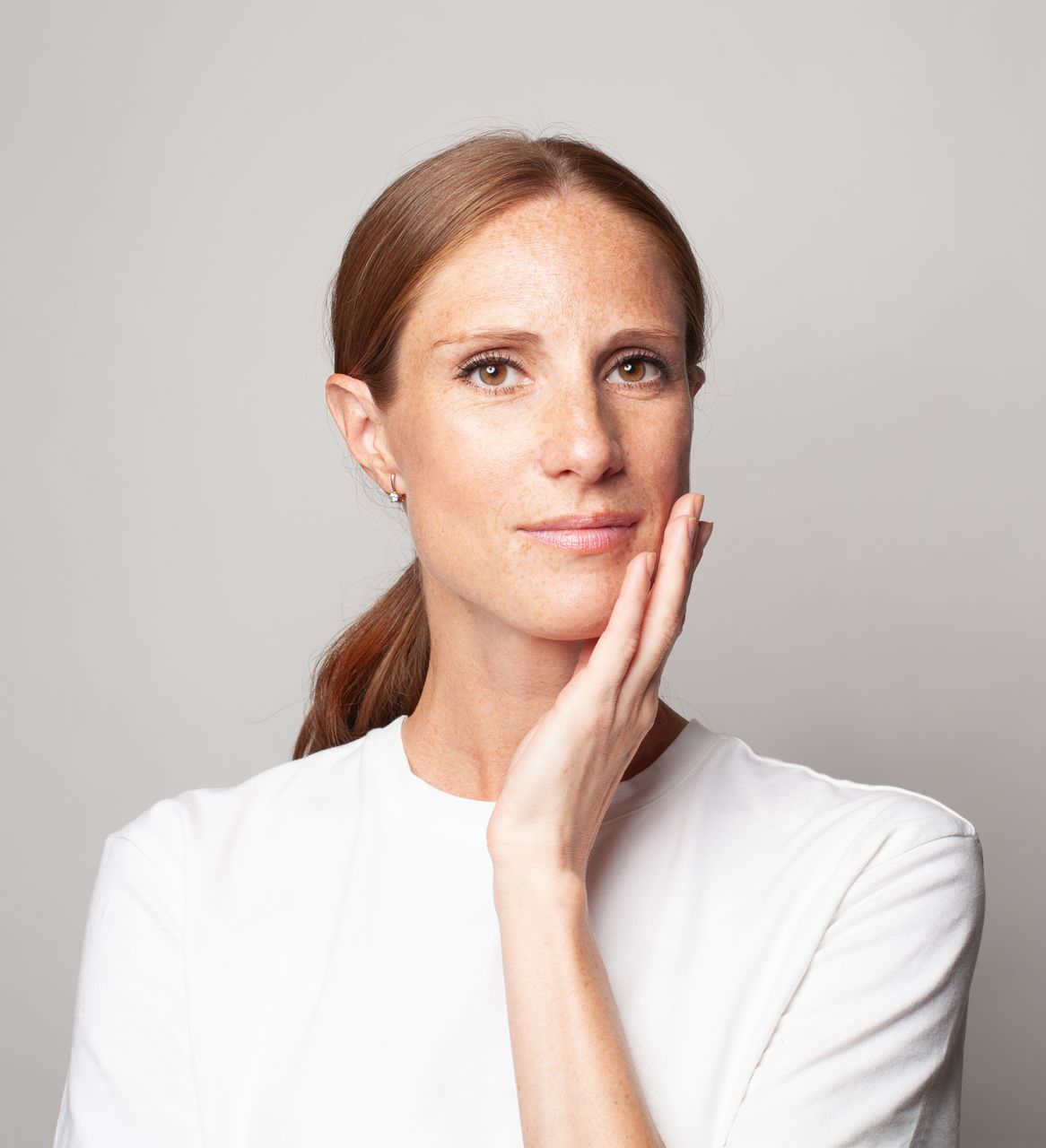 Portrait of a person in a white shirt, touching their cheek against a light gray background