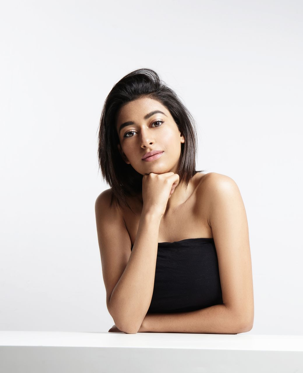 Woman with dark hair resting her chin on her hand against a white background