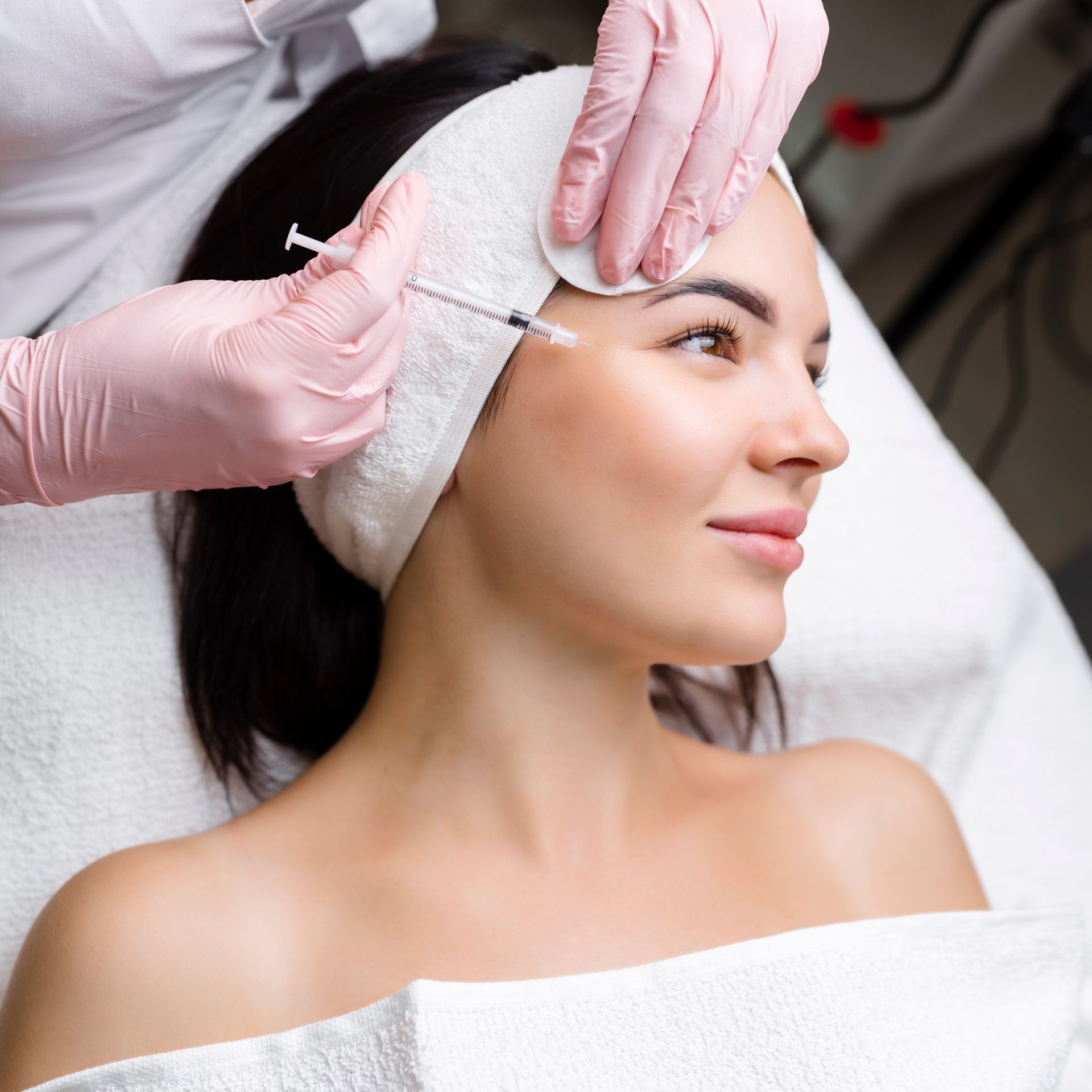 Cosmetician injecting filler into a woman’s forehead during a spa treatment