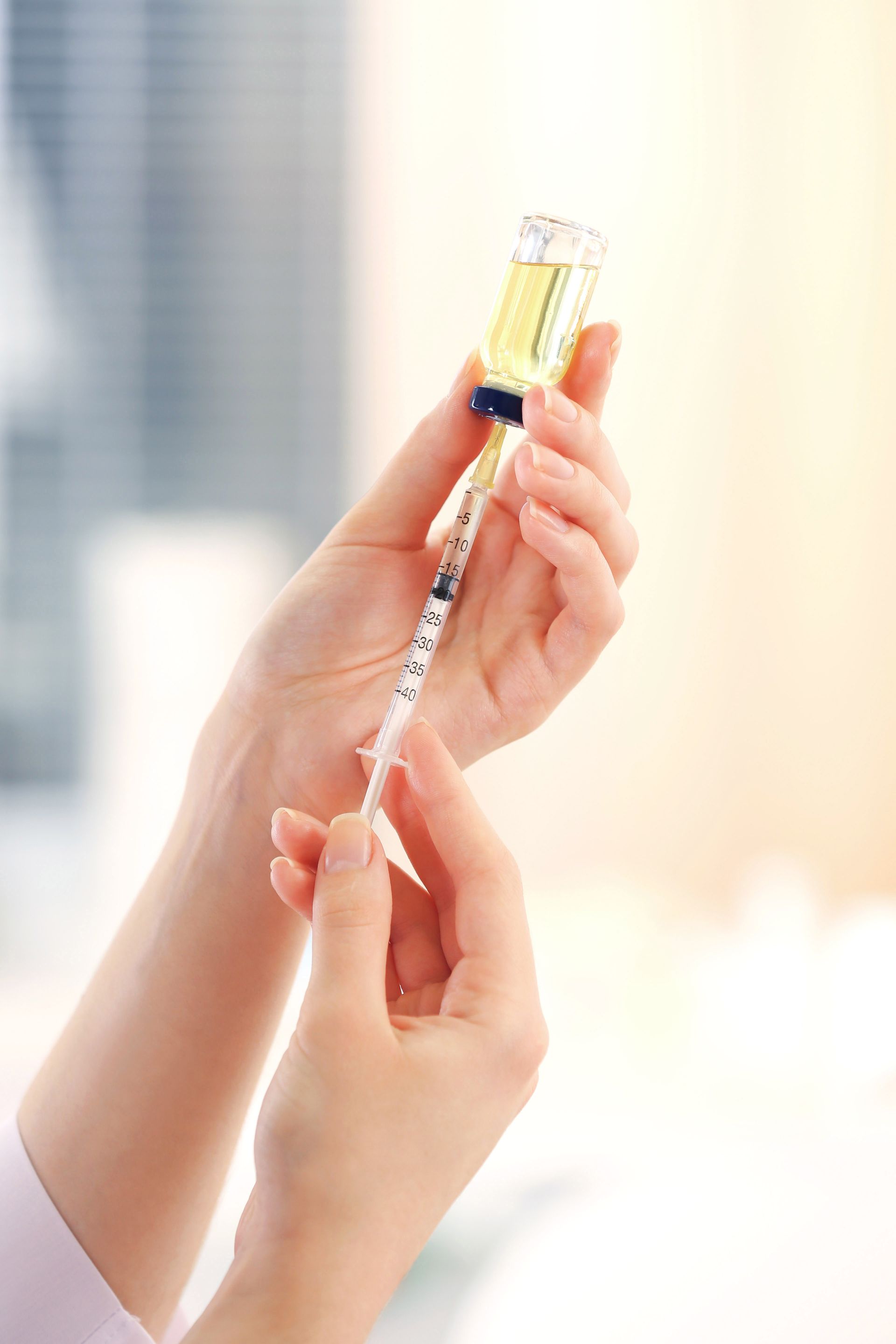 Hands holding a syringe with yellow liquid against a bright blurred background
