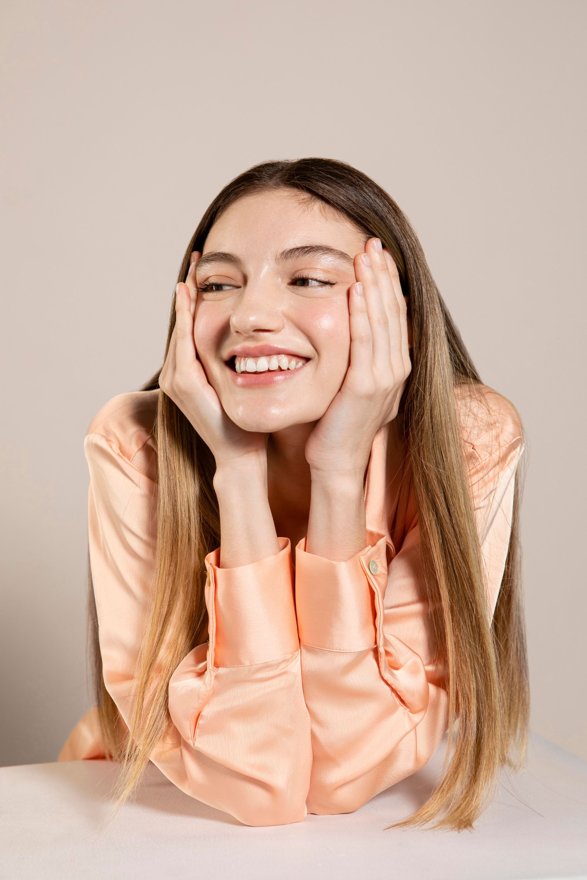 Smiling person in a peach blouse resting their face on their hands at a table