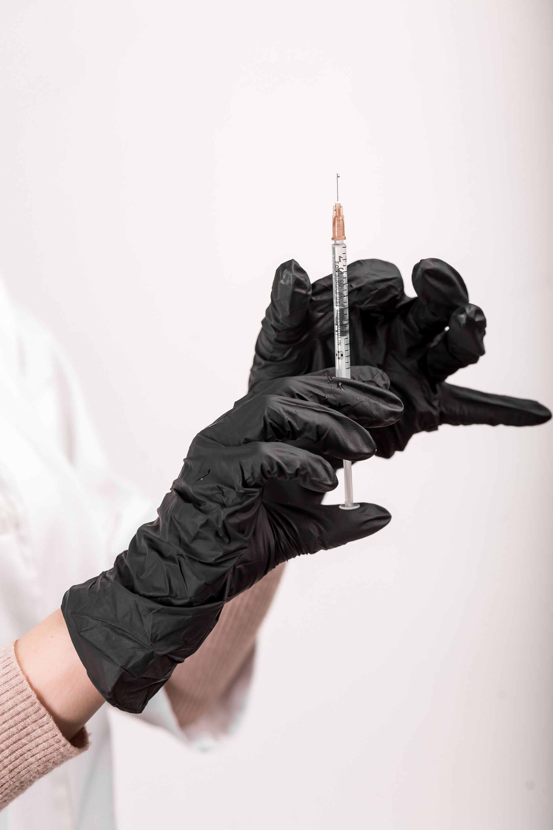 Gloved hand holding a syringe with black ink against a white background