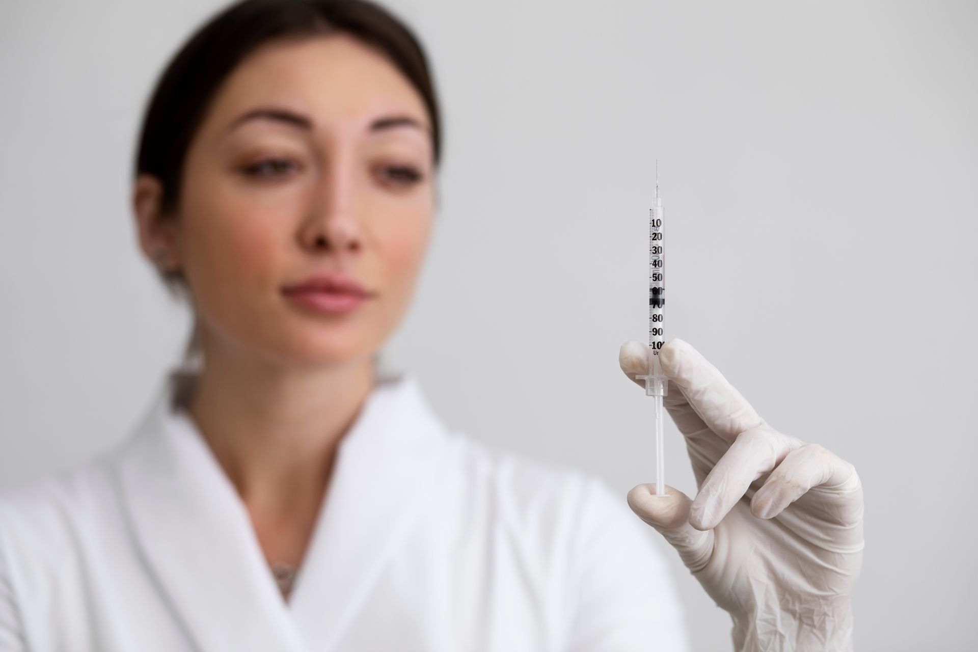 Gloved hand holding a syringe in front of a blurred medical professional in a white coat