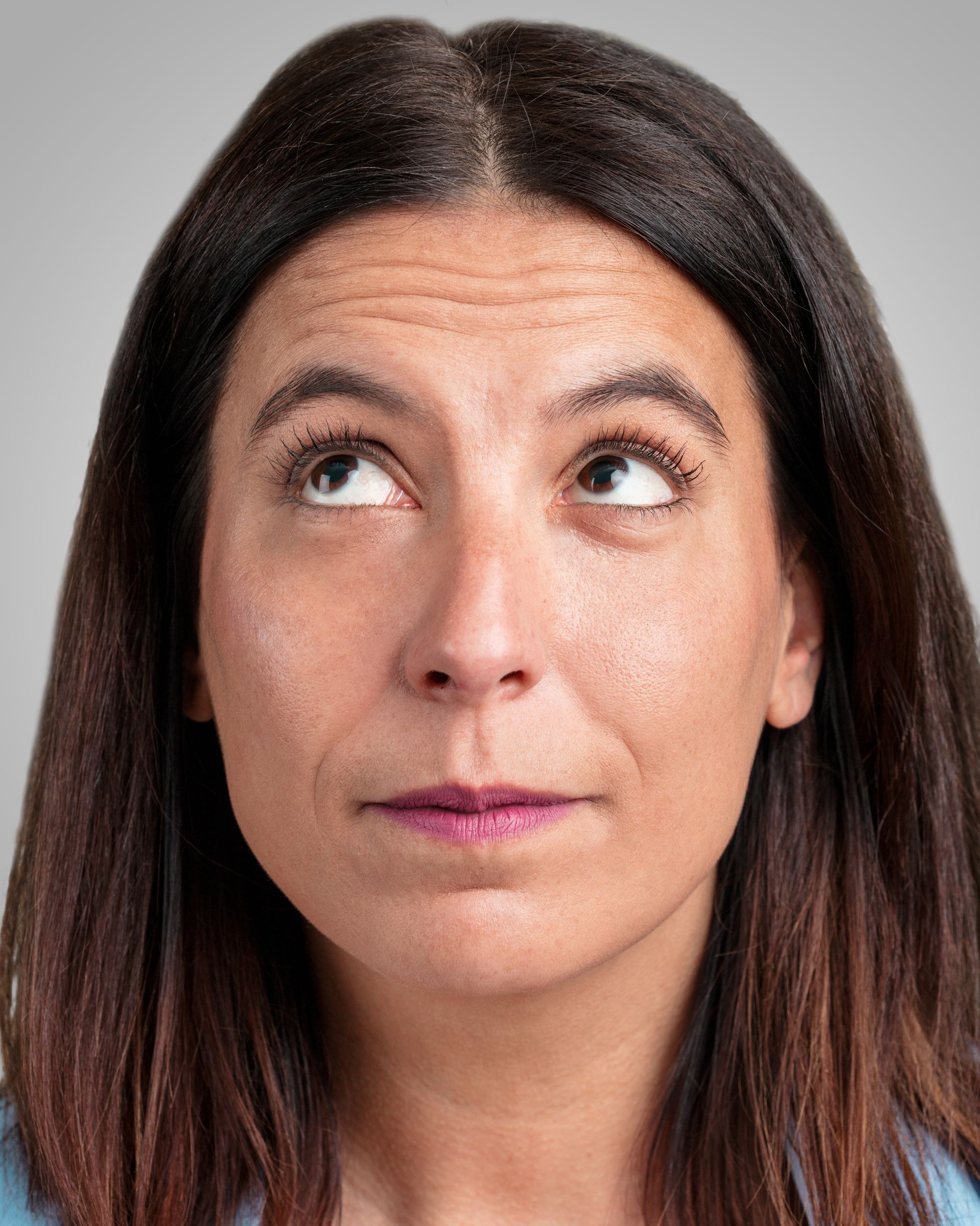 Woman with dark hair looking upward, wearing a neutral expression against a gray background