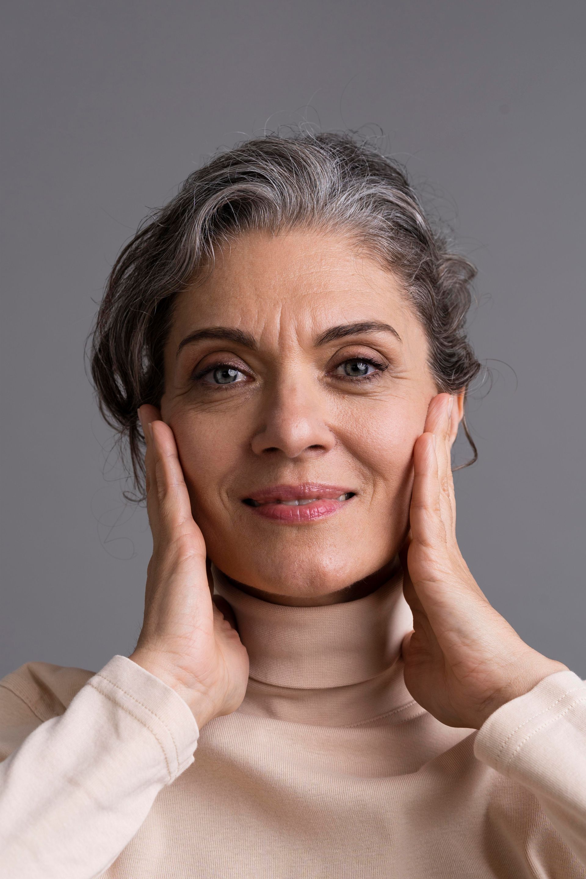 Portrait of a smiling person with hands gently cupping their face against a gray background