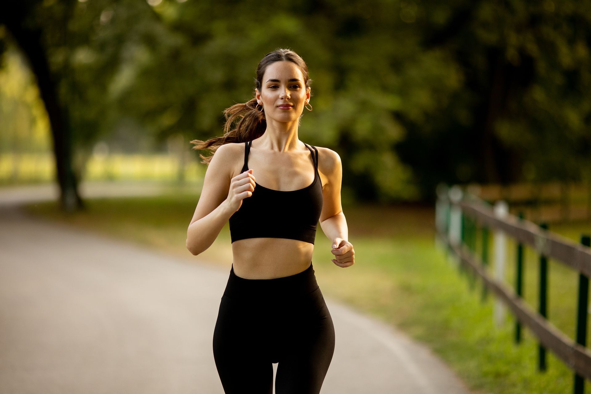Woman jogging on a tree-lined path, wearing a black sports bra and leggings.