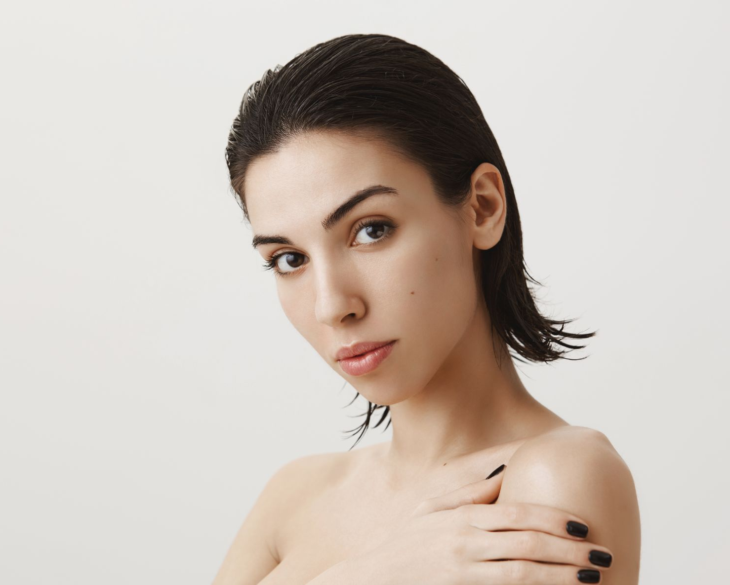 Portrait of a person with wet dark hair, bare shoulders, and a direct gaze against a white background