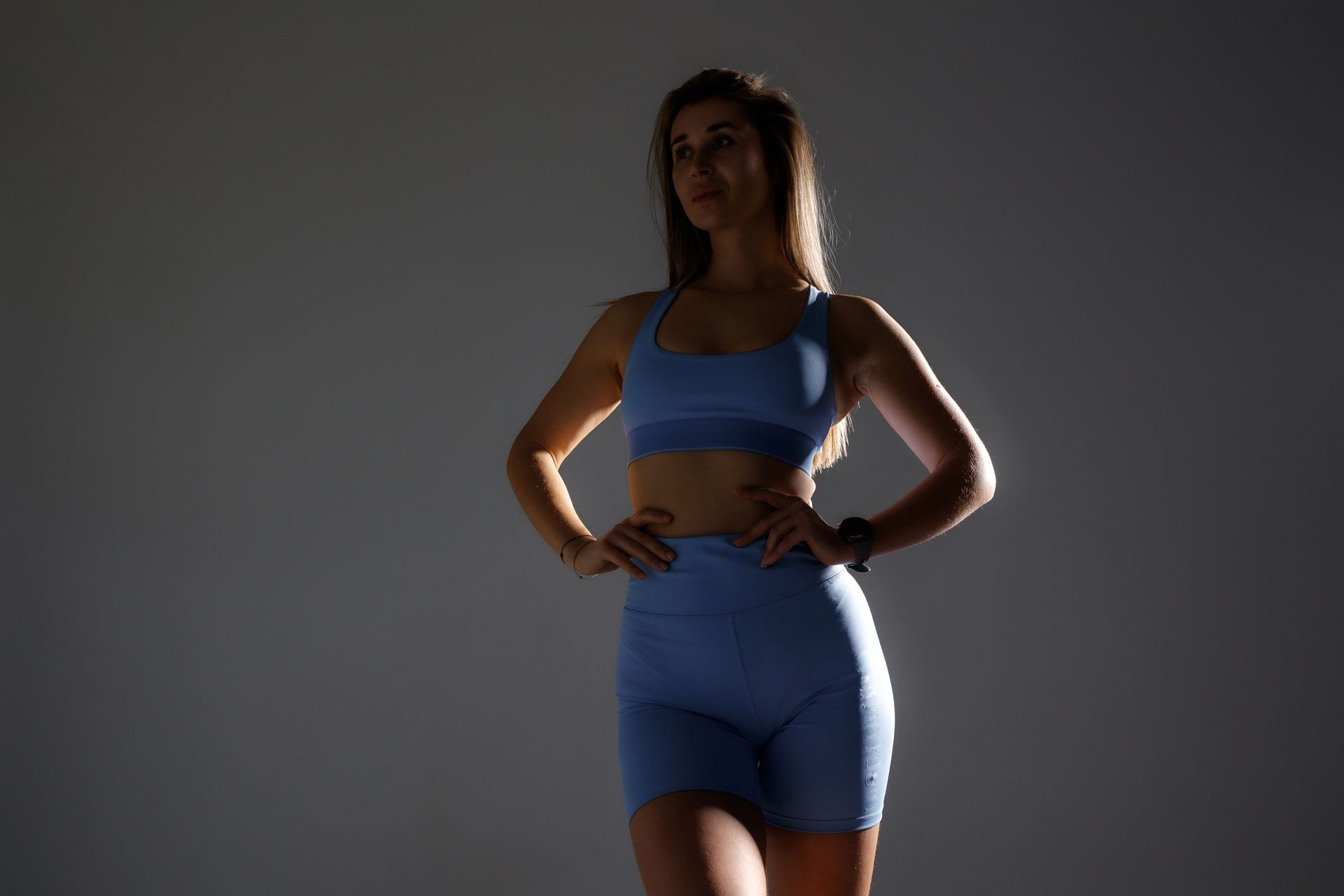 Woman in blue athletic wear standing with hands on hips against a gray backdrop