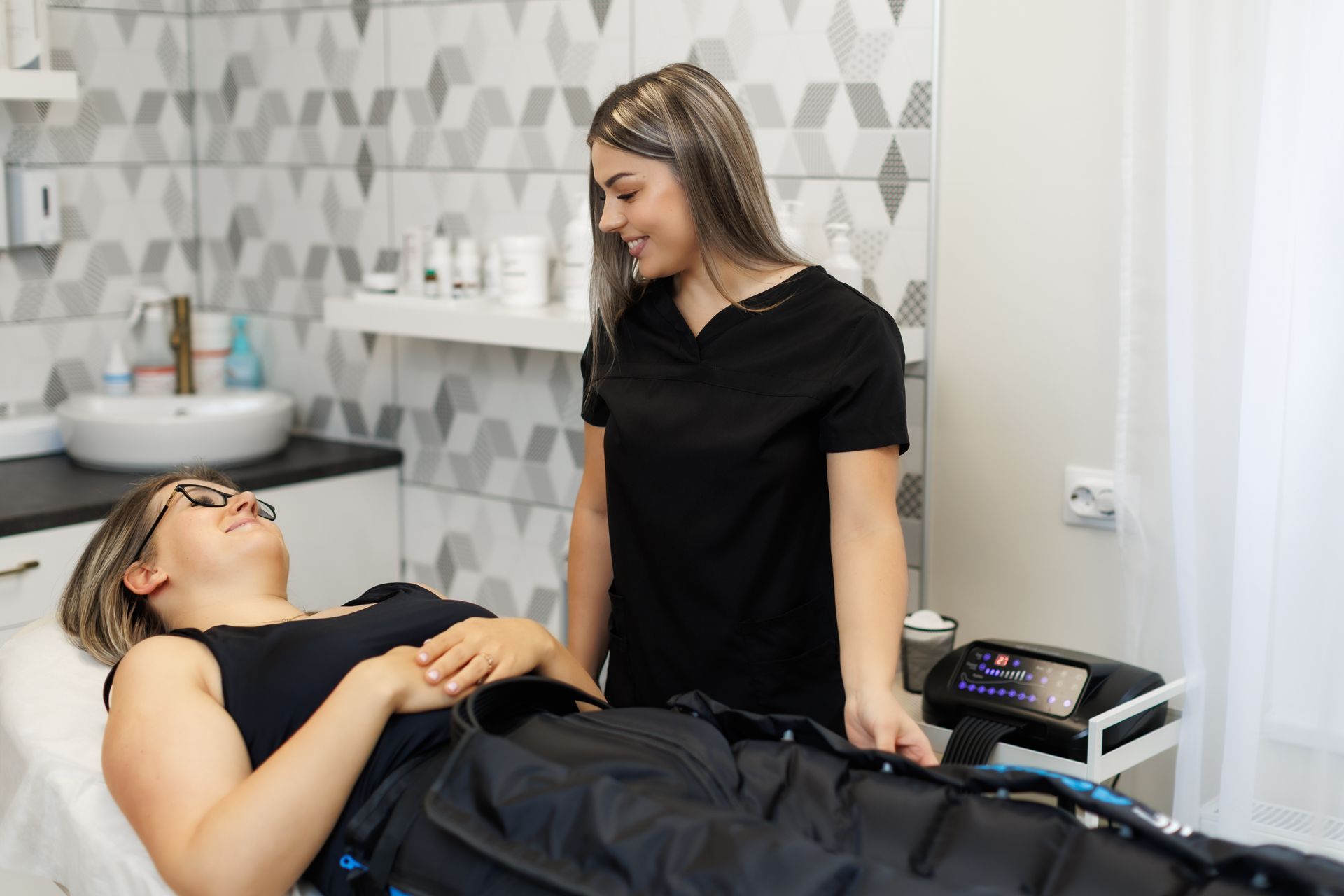 Woman receiving spa treatment while another woman stands beside a massage table in a clinical room