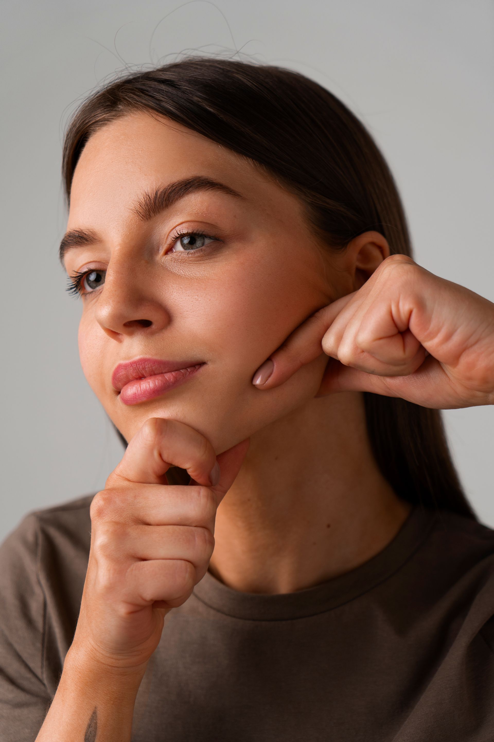 Woman demonstrating facial massage on her cheek, with fingers pressing along the jawline.