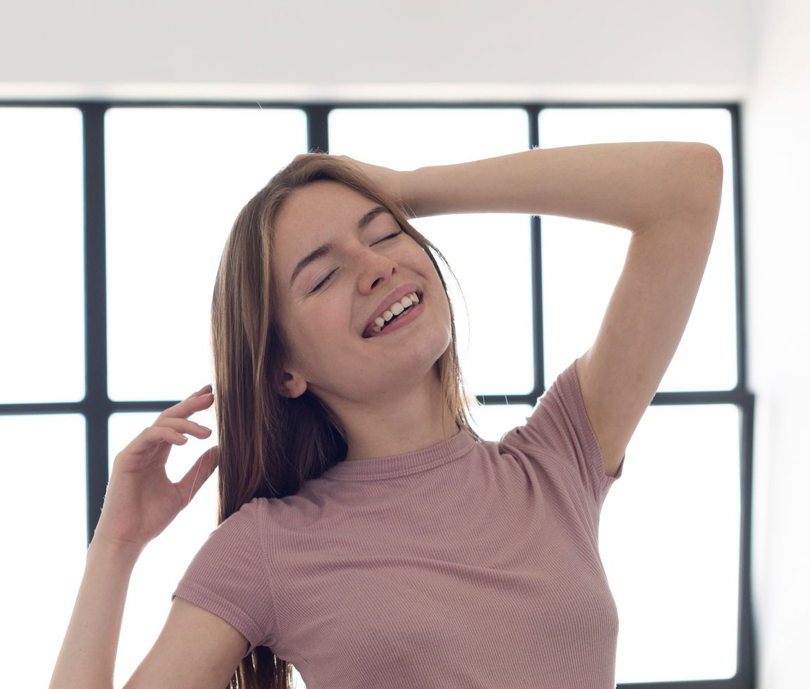 Smiling woman stretching with one arm behind her head in a bright room