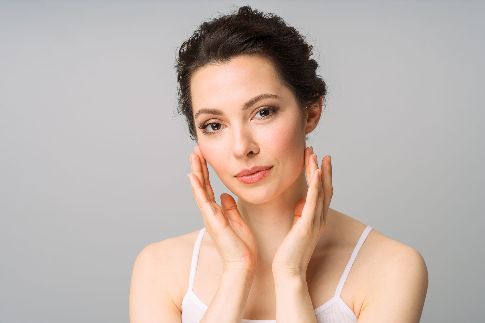 Portrait of a woman with hands on her cheeks against a light gray background