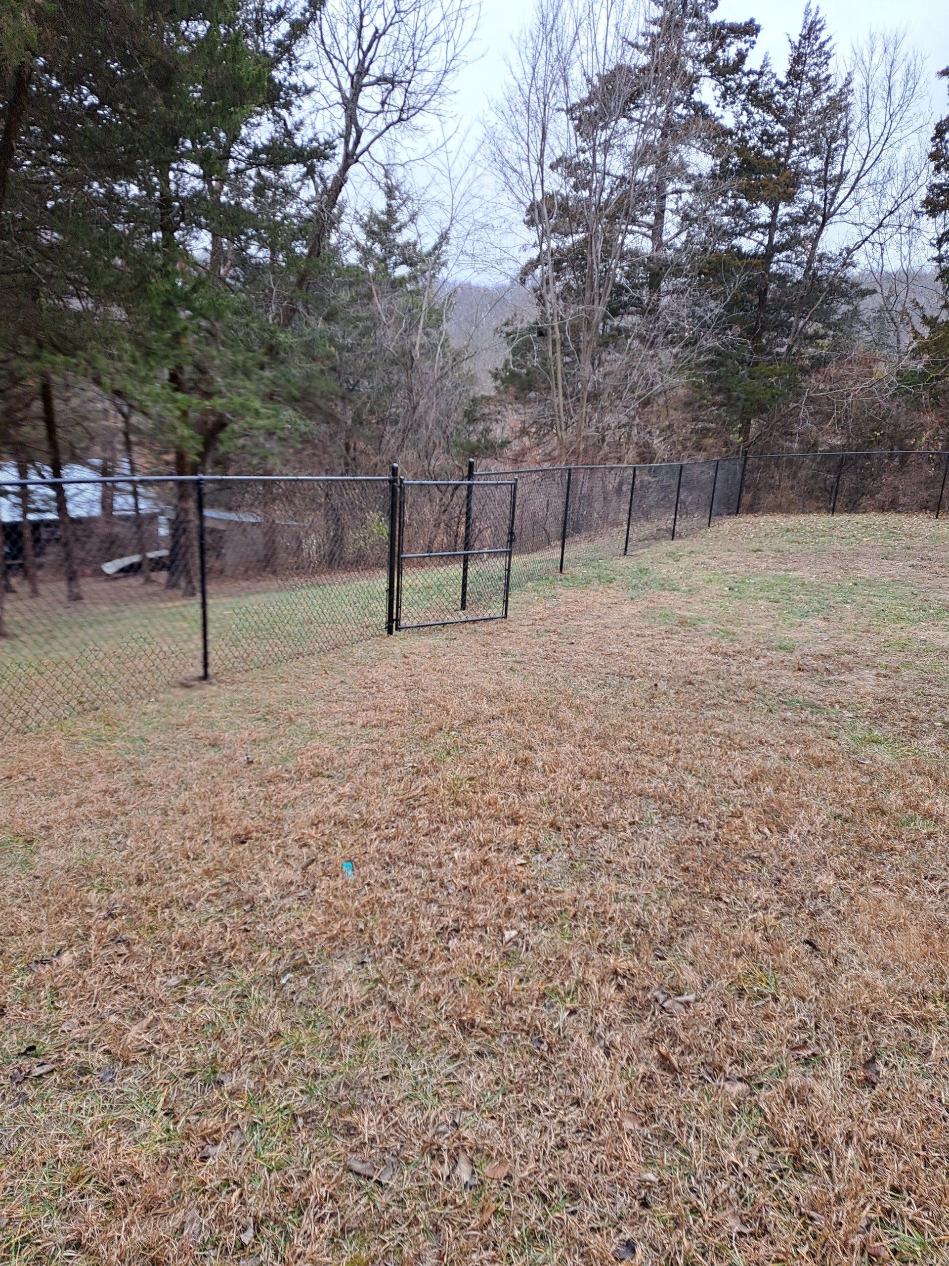 There is a fence in the middle of a field with trees in the background.