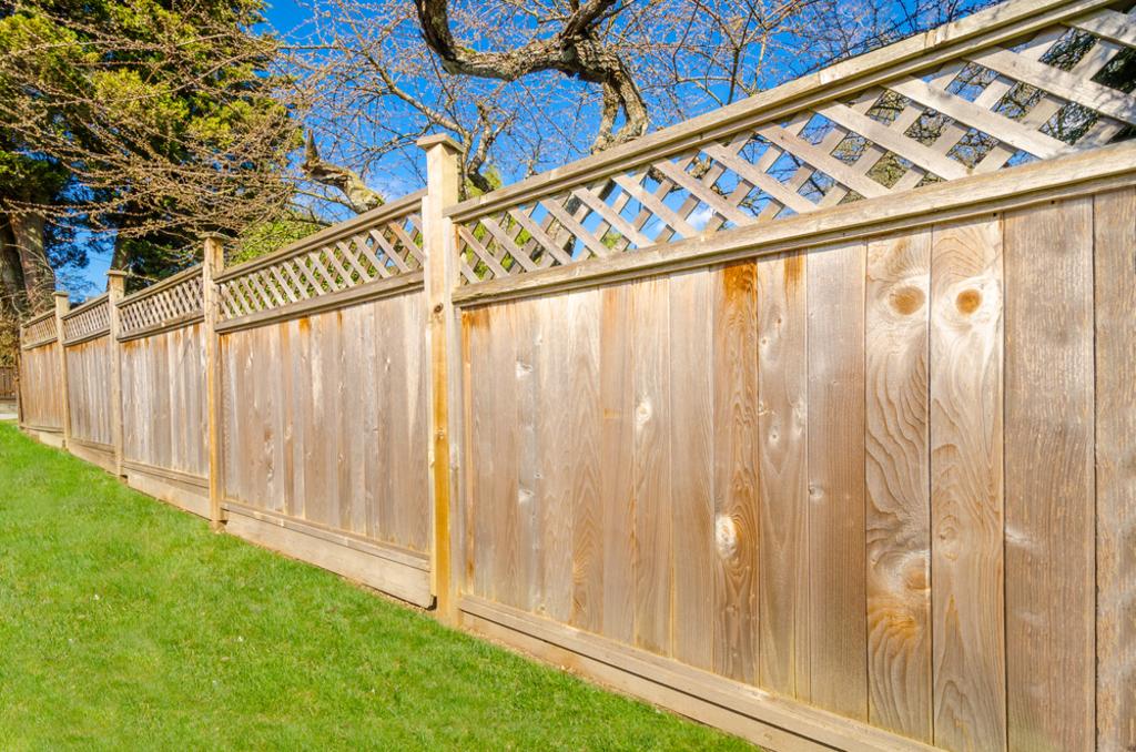 A wooden fence surrounds a lush green lawn with trees in the background.