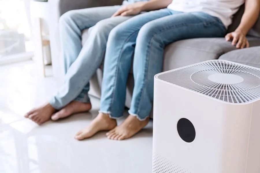 Two People Sit on a Couch, Near an Air Purifier on a White Floor — Climate King In Dubbo, NSW