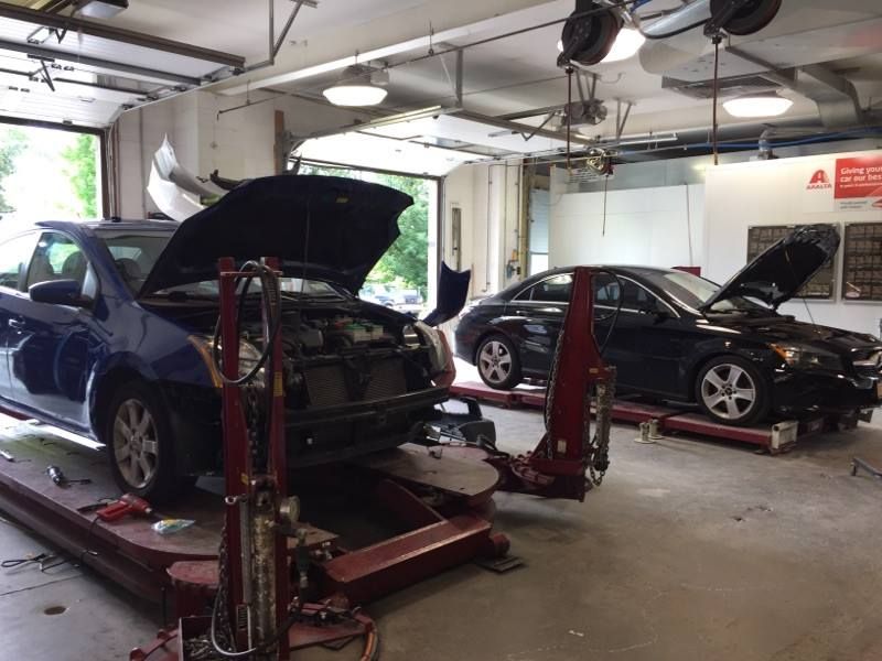 Two cars with open hoods parked on lift platforms inside a well-lit auto repair shop.