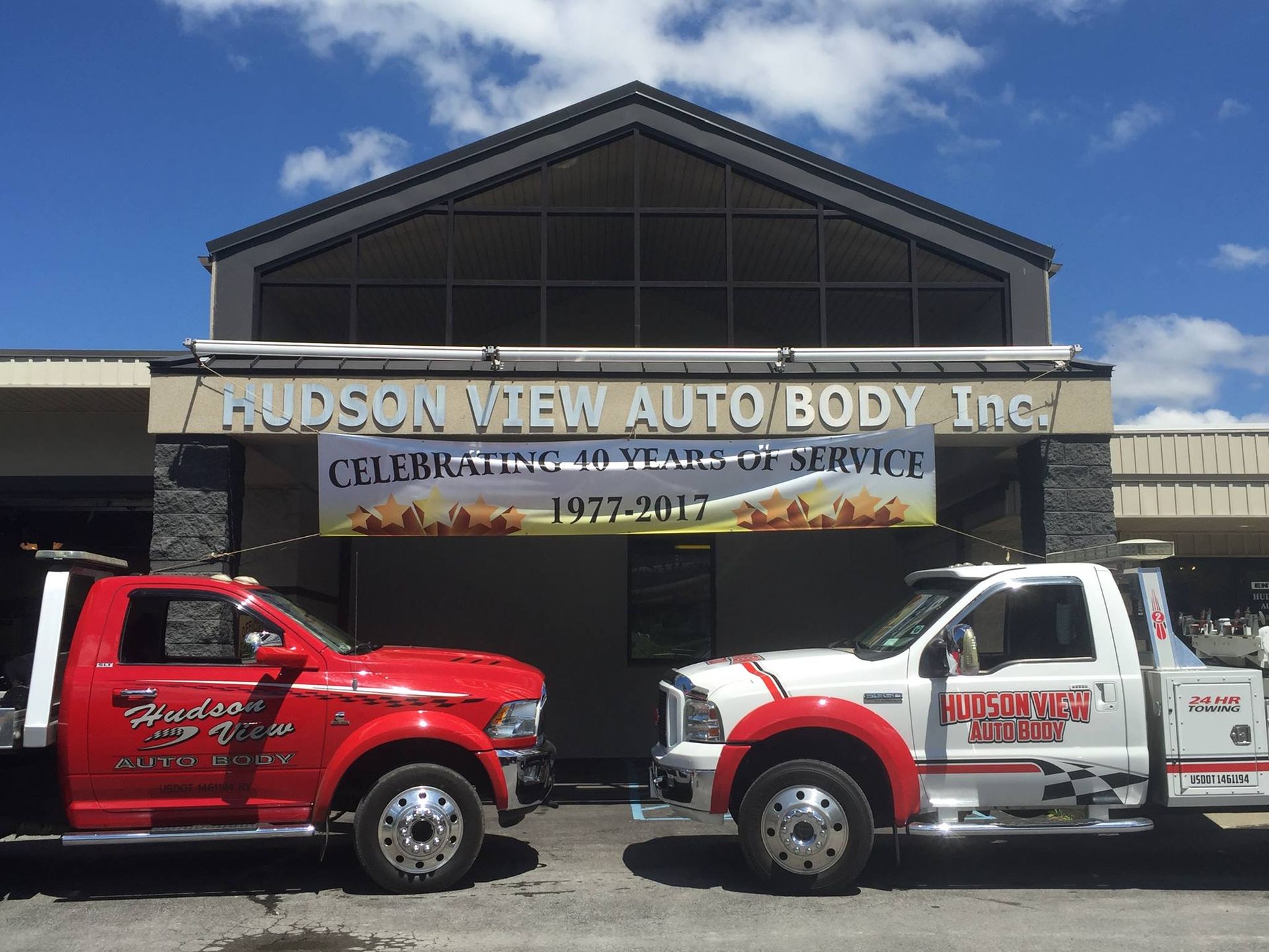 Two tow trucks, one red and one white, parked in front of Hudson View Auto Body, Inc. featuring a 40-year anniversary banner.