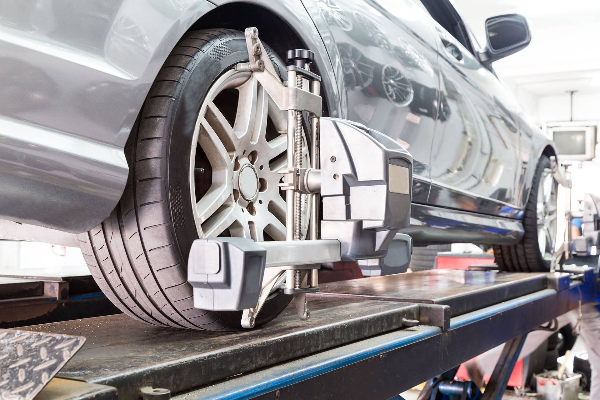 A silver car elevated on a service rack with a diagnostic alignment sensor mounted to the rear wheel.