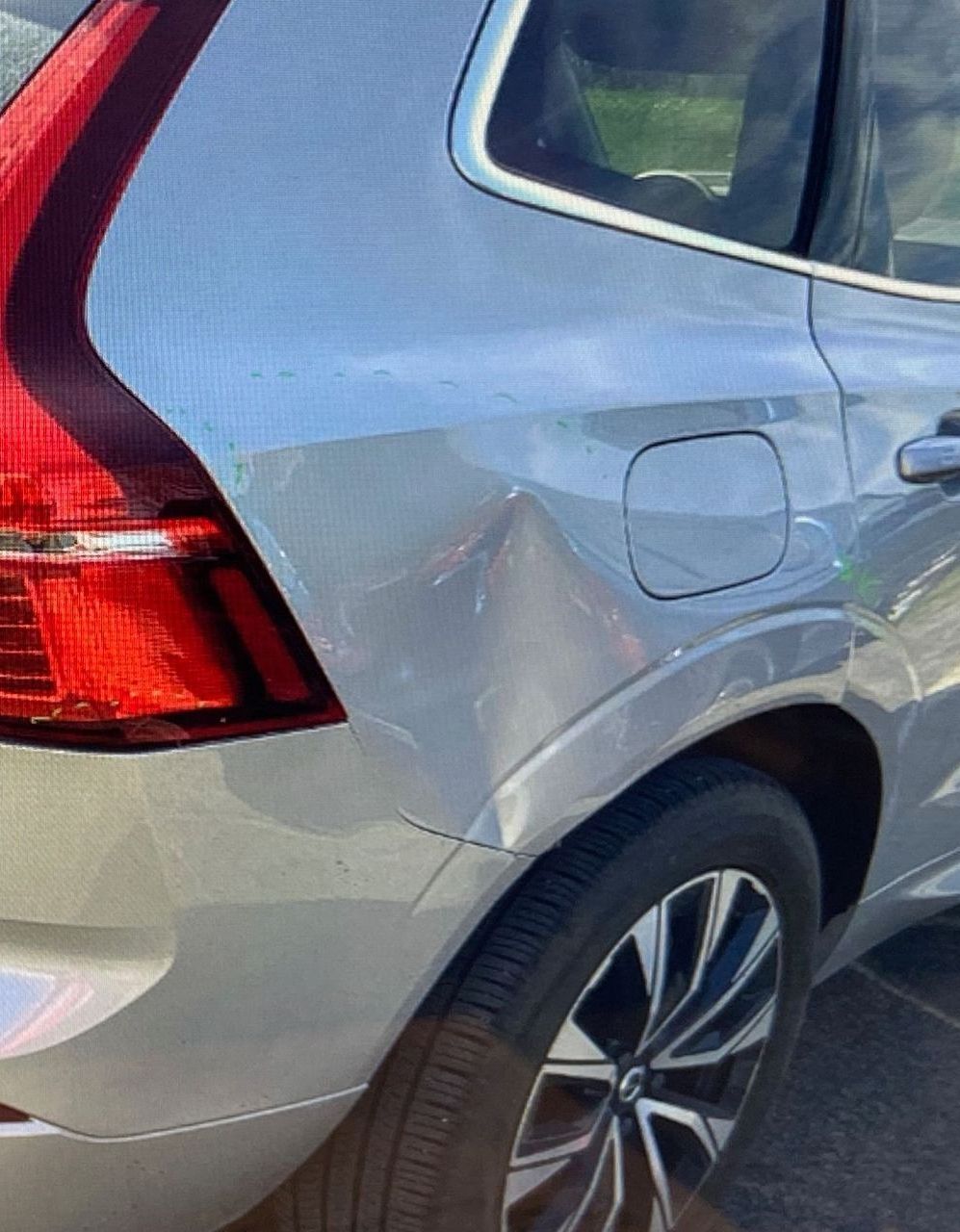 A silver SUV with a dented rear quarter panel located near the tail light and fuel door.