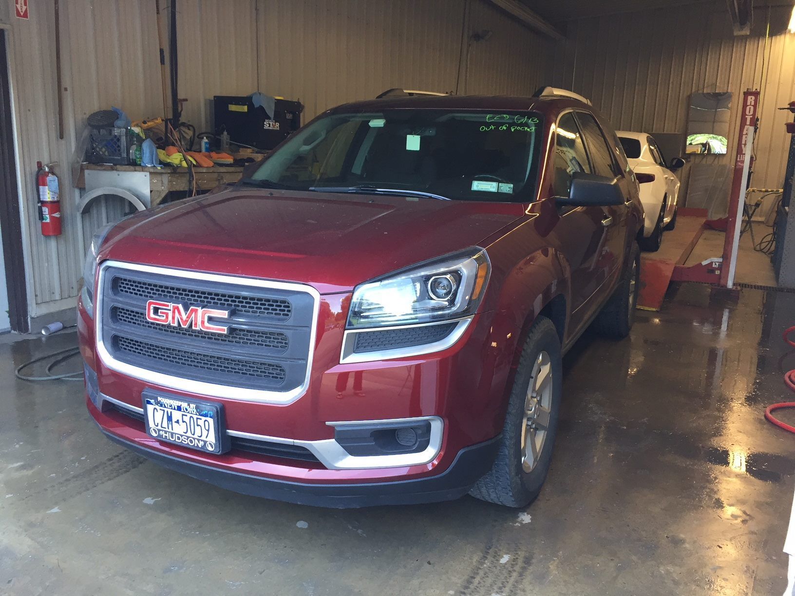 A red GMC Acadia SUV parked inside a garage or auto repair shop.
