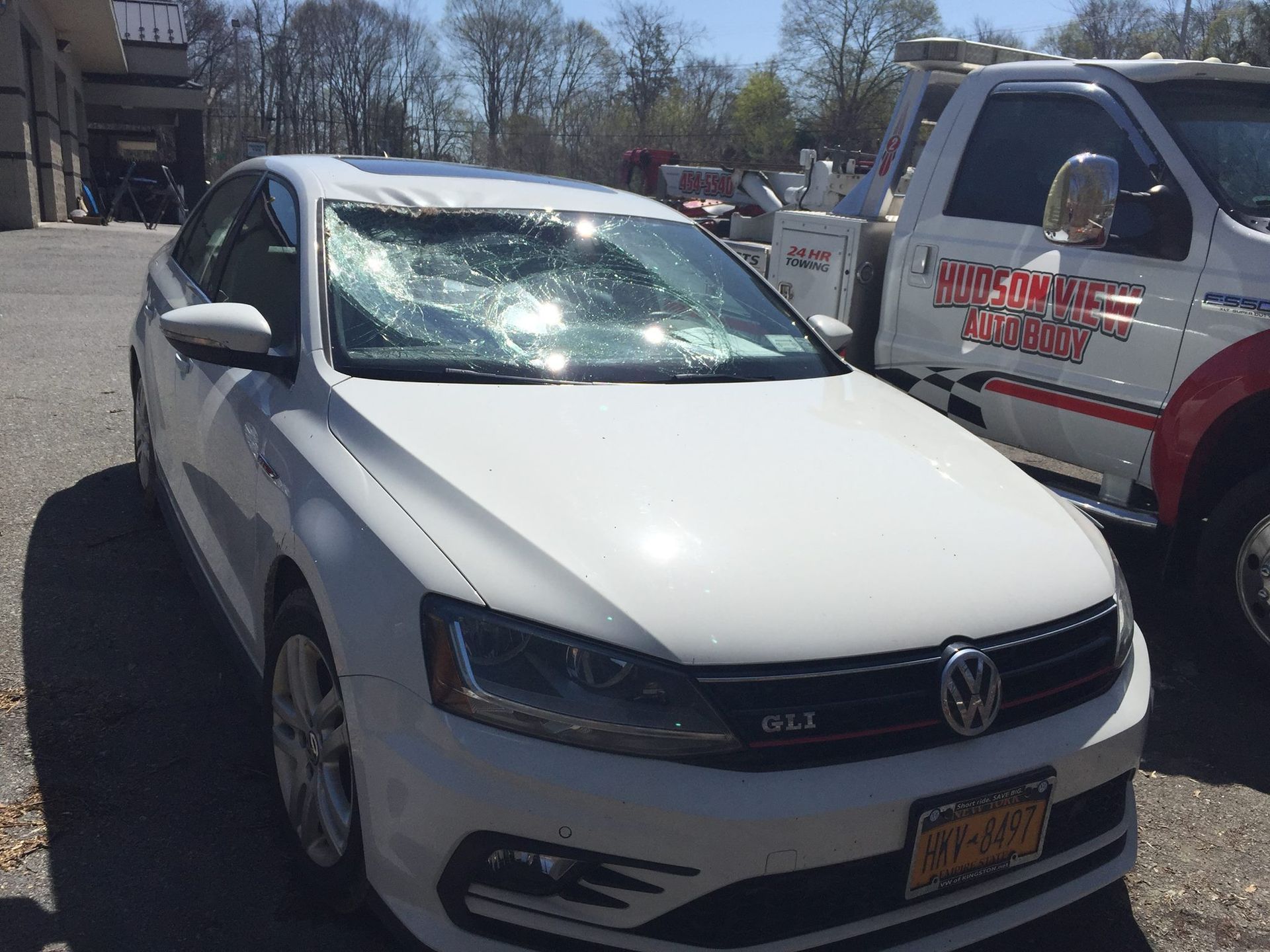 A white Volkswagen GLI with a shattered windshield parked next to a white tow truck.