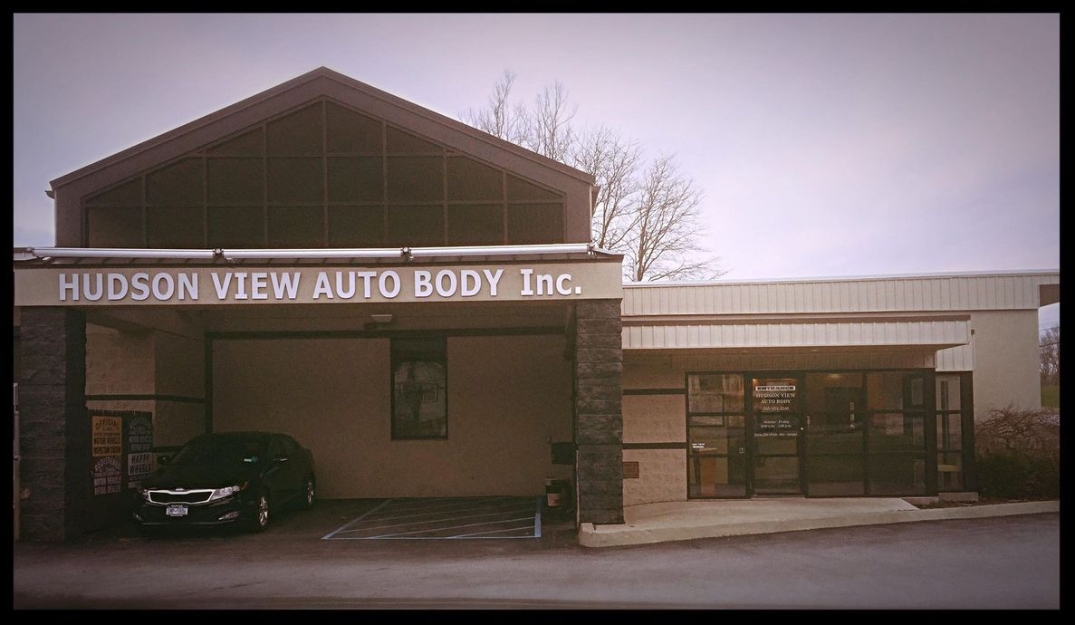 Exterior of Hudson View Auto Body Inc. featuring a peaked roof, stone pillars, and a black car parked under the overhang.