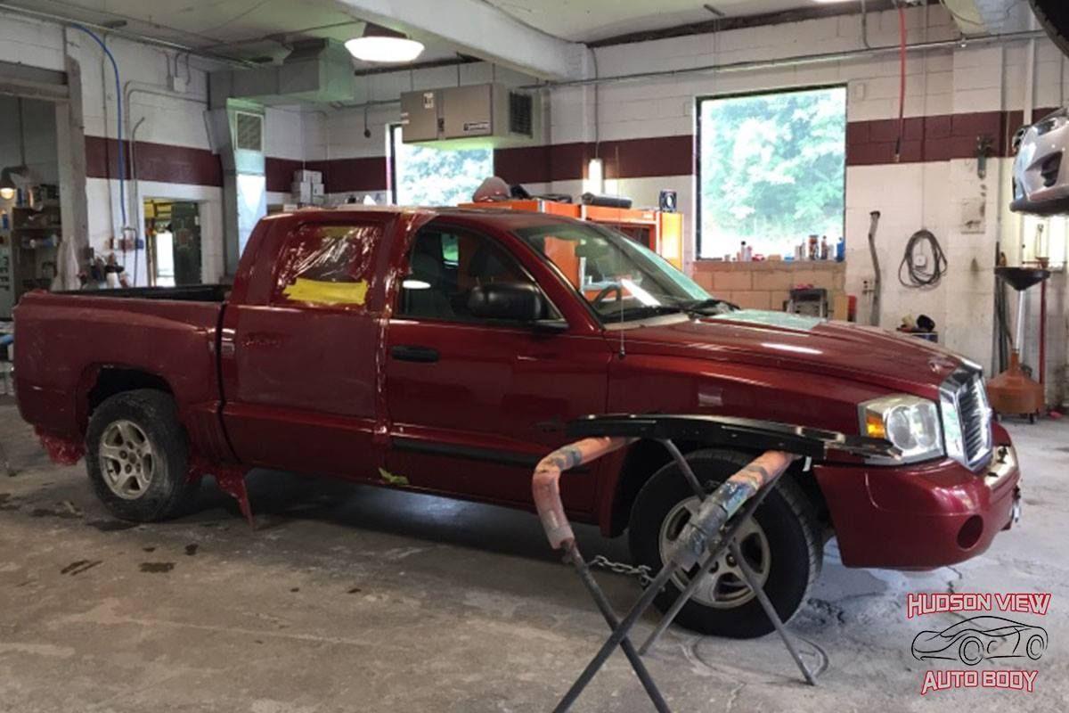A red crew cab pickup truck parked inside a bright auto body repair shop.
