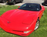 A bright red C5 Chevrolet Corvette parked on a patch of green grass.