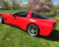 A bright red Corvette sports car parked on a green lawn with blooming trees in the background.