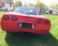 A bright red Chevrolet Corvette parked on a grassy lawn, viewed from the rear, showing its distinctive tail lights.