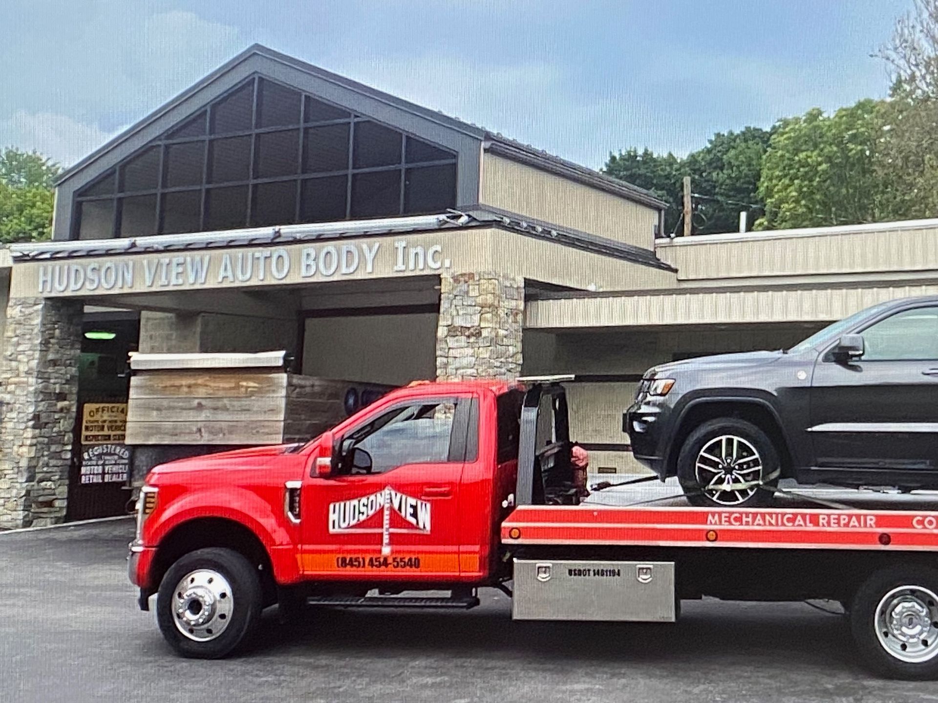 A bright red flatbed tow truck is parked in front of the Hudson View Auto Body Inc. building.