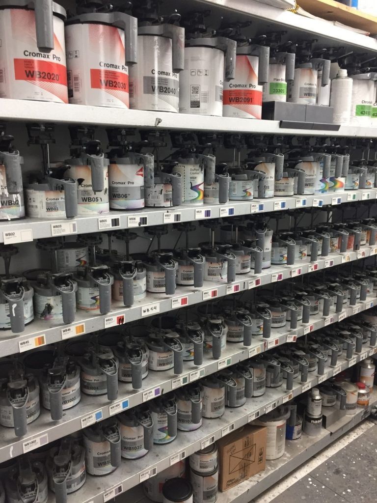 Many cans of paint with handles arranged on rows of shelves in a hardware store or paint mixing station.