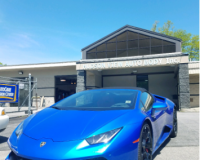 A bright blue Lamborghini convertible parked in front of a modern, single-story commercial building under a clear blue sky.