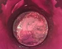 A top-down view of a dark pink container holding a translucent, jelly-like substance with small bubbles.